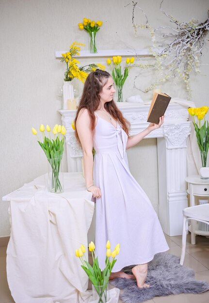 Foto een meisje in een witte jurk en met lang haar leest een boek tegen een achtergrond van gele bloemen