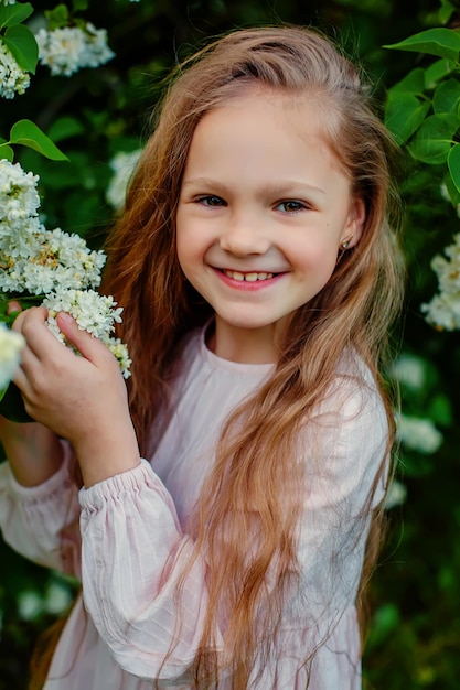 Een meisje in een witte jurk glimlacht voor een bos witte bloemen.