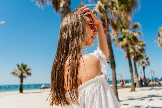 Een meisje in een witte jurk staat op een strand en kijkt naar de camera.