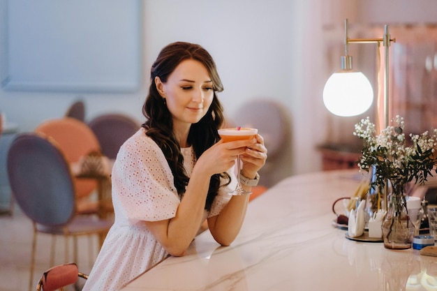 Een meisje in een witte jurk zit aan de bar in een café en drinkt een cocktail