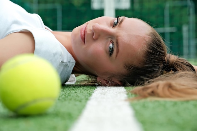 Een meisje in een witte sportjurk ligt op de tennisbaan, tennisbaan en racket