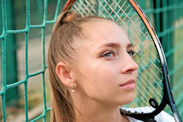 Een meisje in een witte sportjurk staat of zit op een tennisbaan in de buurt van het netportret van een meisje op de tennisbaan