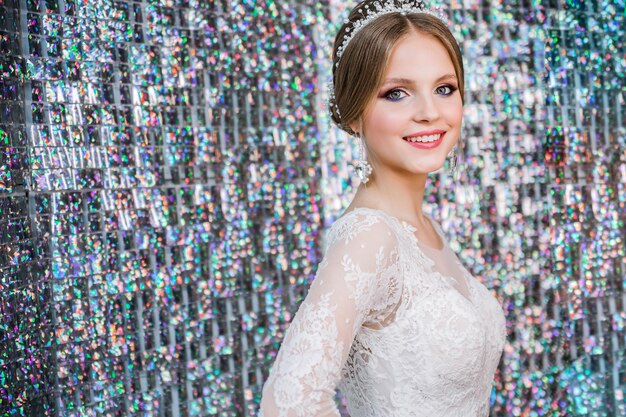 Een meisje in een witte trouwjurk met een open rug make-up een kapsel in de vorm van een stel poses op glittergordijn zilveren achtergrond