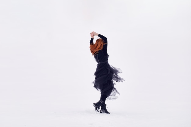 Een meisje in een zwarte jas met rood haar danst in de witte sneeuwxA
