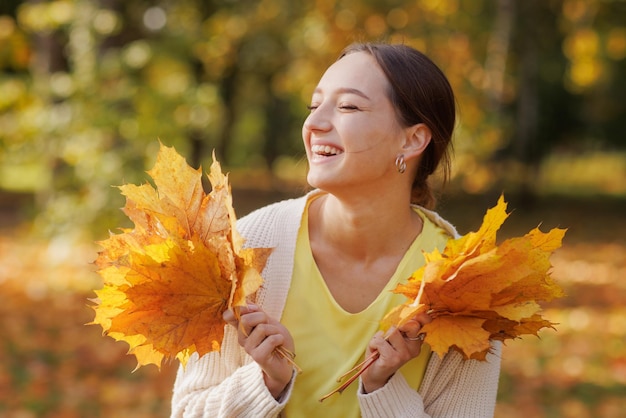 een meisje in gele kleren in een herfstpark verheugt zich in de herfst met gele bladeren in haar handen