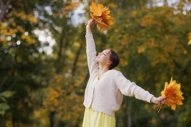 Foto een meisje in gele kleren in een herfstpark verheugt zich in de herfst met gele bladeren in haar handen