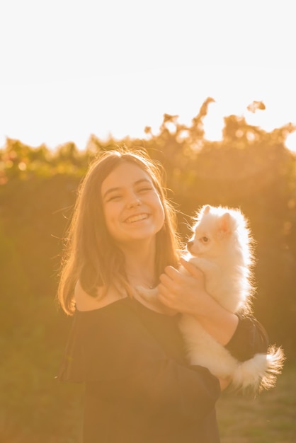 Een meisje in haar armen met een witte Spitz-hond. Tienermeisje lachen. Dieren, huisdieren en mensen.