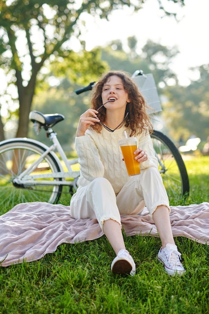 Een meisje in het wit dat op een gras in het park zit en er ontspannen uitziet