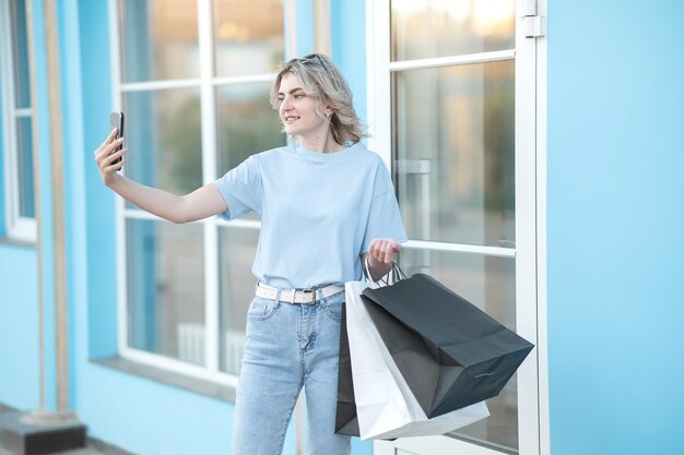 Een meisje in jeans met tassen in haar handen verlaat de winkel in de zomer kijkt naar de telefoon