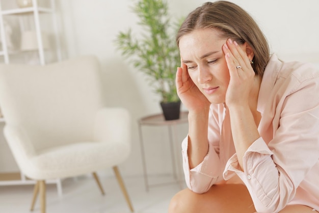 Een meisje in lichte kleding lijdt aan hoofdpijn door migraine aan haar slapen vast te houden