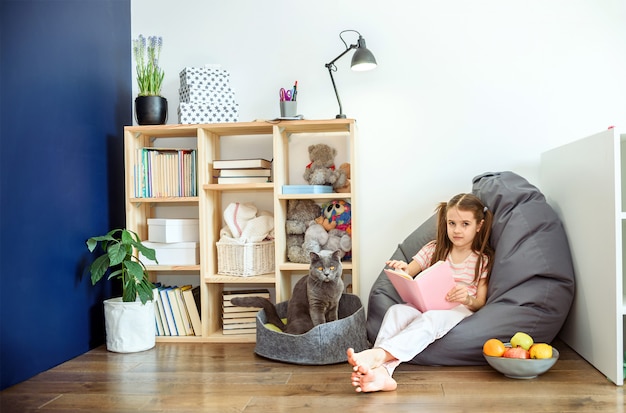 Een meisje in medisch masker die op houten vloer situeren en boeken lezen tijdens quarantaine