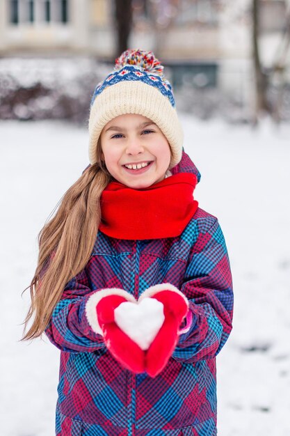 Een meisje in rode handschoenen houdt een hartvormig sneeuwbalsymbool van liefde vast