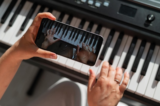 Een meisje kijkt naar een online muziekles op een smartphone en leert piano spelen Close-up van woman39s handen op toetsen