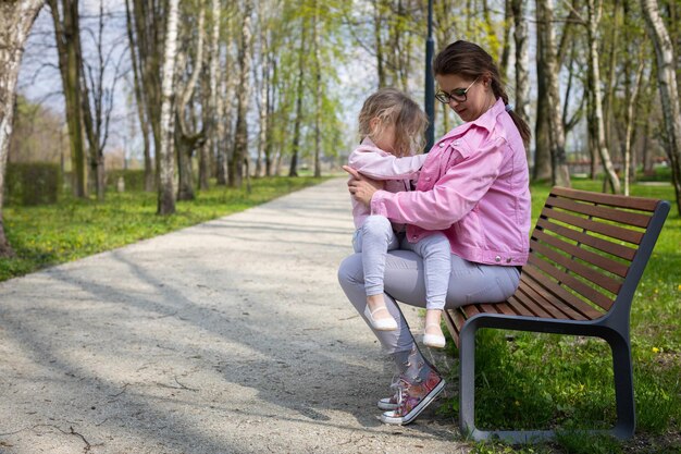 Een meisje kijkt naar haar moeder achter haar jas die in het park op een bankje rust.