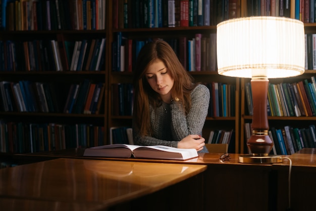 Een meisje leest een boek in een bibliotheek terwijl ze aan een tafel zit