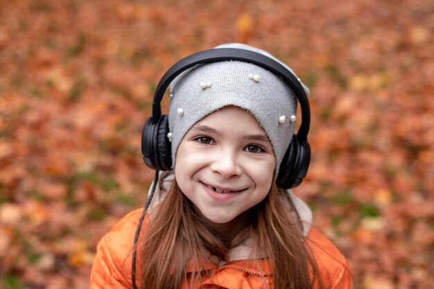 Een meisje luistert naar muziek op koptelefoon in een herfstpark en kijkt naar de camera