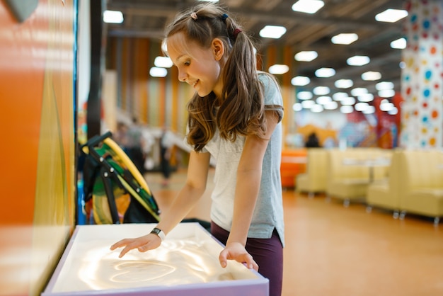 Een meisje maakt een zandfoto in het uitgaanscentrum. Vrouwelijke kinderen vrije tijd op vakantie, geluk jeugd, gelukkige kinderen op speelplaats