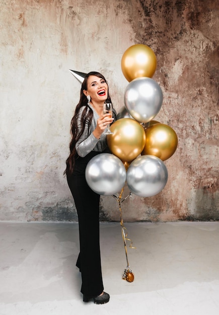 Een meisje met ballonnen lacht tegen de achtergrond van een decoratieve muur Een mooie gelukkige vrouw op de verjaardag van een nieuwjaarsfeestje met plezier met een glas champagne