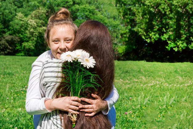 Een meisje met blond haar in een knot gekamd, geeft haar moeder een boeket witte bloemen voor Moederdag. 26 mei.