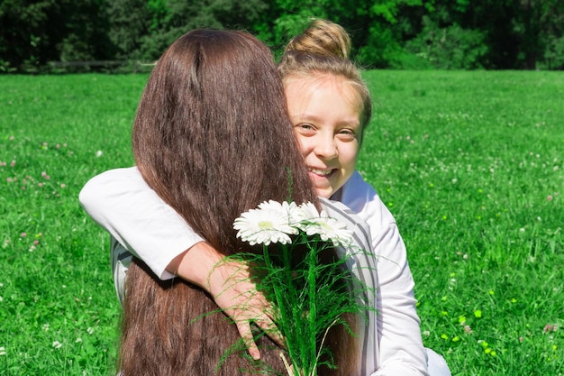 Een meisje met blond haar in een knotje geeft haar moeder een boeket witte bloemen