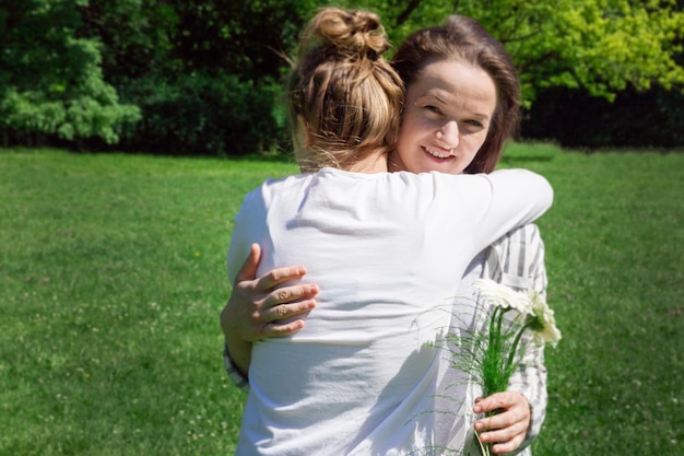 Een meisje met blond haar in een knotje geeft haar moeder een boeket witte bloemen