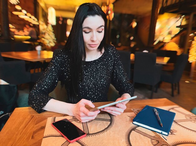 Een meisje met donker haar werkt in een café met een tablet, een telefoon en een notebook in de buurt. Coworking, workfloworganisatie. Bedrijfsconcept.