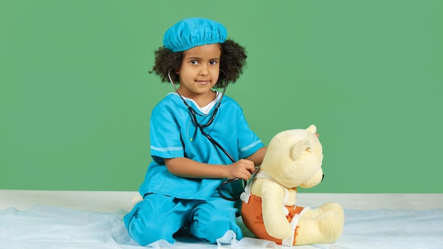 Een meisje met een afro-amerikaans uiterlijk in een dokterskostuum behandelt haar teddybeer