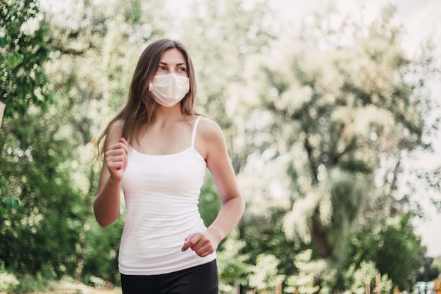 Een meisje met een beschermend ademhalingsmasker rent door het park tussen groene bomen en kijkt naar de kopieerruimte, quarantaine, coronavirus 2020