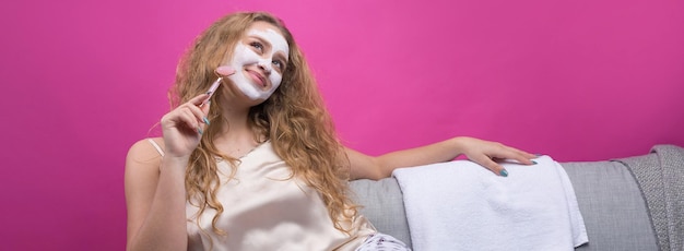 Een meisje met een cosmetisch masker op haar gezicht zit op de bank