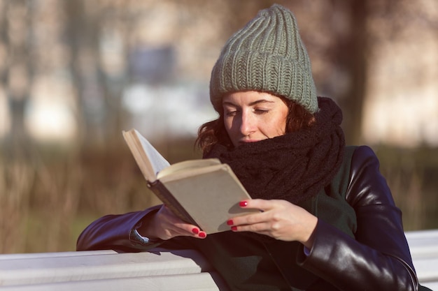 Een meisje met een hoed zit op een bankje in het park en leest een boek Ontspannen in de natuur