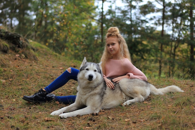 Een meisje met een husky loopt in het bos.