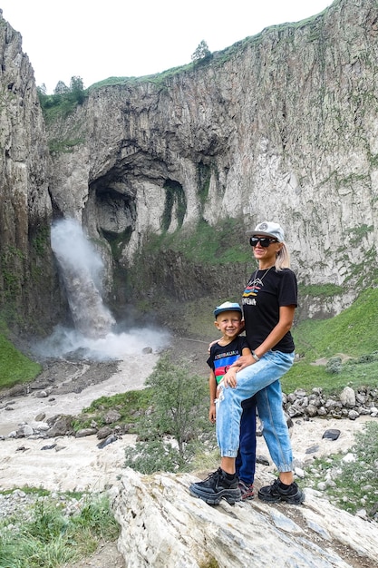 Een meisje met een kind op de achtergrond van de tuzlukshapa-waterval op het grondgebied van kabardinobalkarië kaukasisch