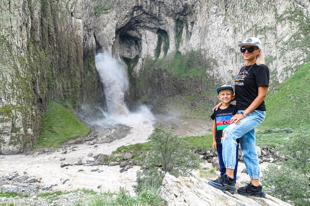 Een meisje met een kind op de achtergrond van de TuzlukShapa-waterval op het grondgebied van KabardinoBalkarië Kaukasisch