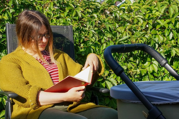 Een meisje met een kinderwagen leest een boek in de natuur op een zonnige zomerdag