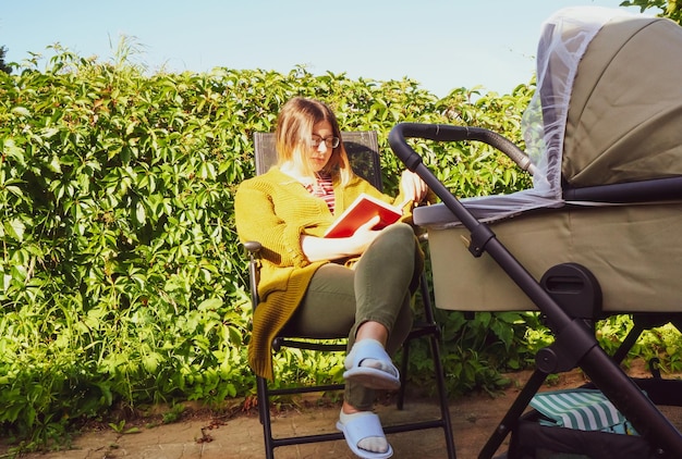 Een meisje met een kinderwagen leest een boek in de natuur op een zonnige zomerdag
