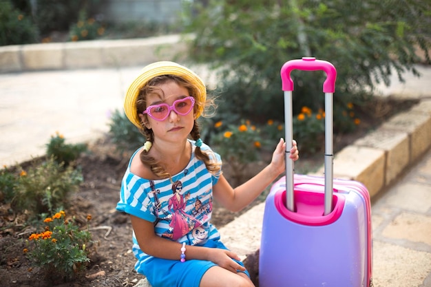 Een meisje met een koffer, een hoed en een zonnebril gaat op vakantie Wachtend op de aankomst van de reis op de woonplaats van het hotel