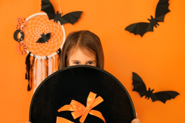 Een meisje met een kwaadaardige blik kijkt uit vanachter een grote heksenhoed in afwachting van Halloween