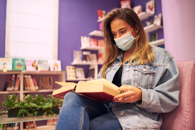 Een meisje met een masker zit een boek te lezen met een paarse achtergrond