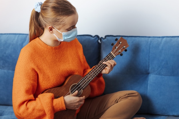 Een meisje met een medisch masker speelt de ukelele