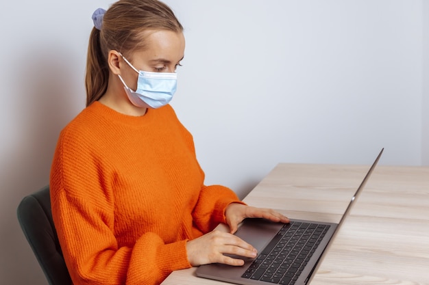 Een meisje met een medisch masker werkt met een laptop