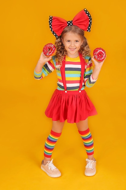 een meisje met een rode strik in een rode rok een gekleurde blouse houdt roze donuts in haar handen