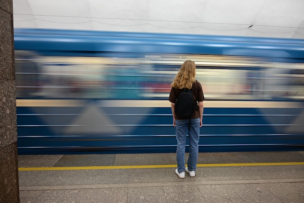 een meisje met een rugzak wacht op een trein op het stationReiziger meisje met een rugzak zit en wacht op de trein op het station Outdoor avontuurlijke reizen per trein concept