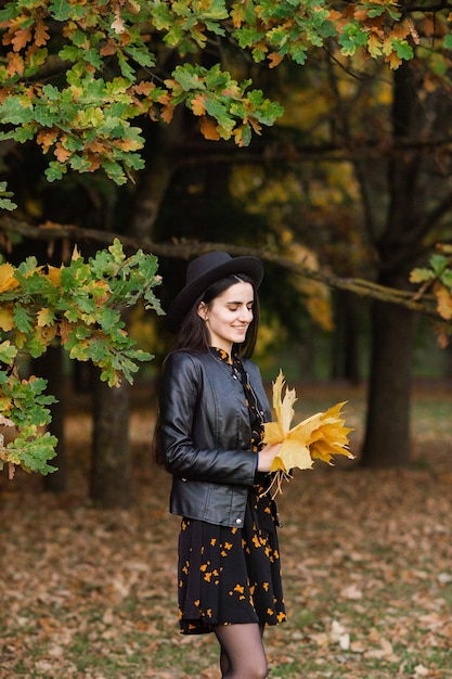 Een meisje met een zwarte hoed houdt gele herfstbladeren in haar handen