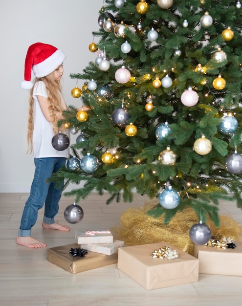 Een meisje met geschenken speelt in de buurt van de kerstboom. Woonkamer interieur met kerstboom en versieringen. Nieuwjaar. Cadeaus geven.