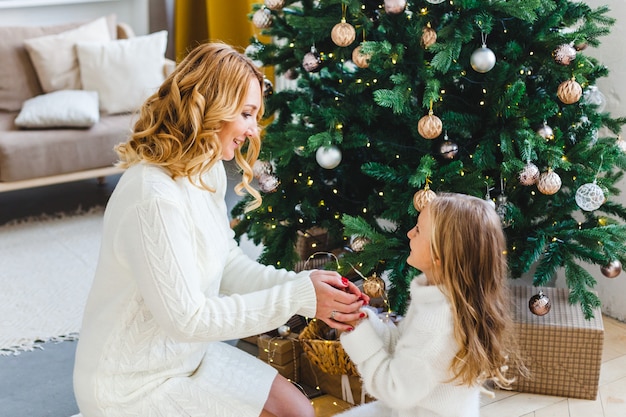 Een meisje met haar moeder in de buurt van de kerstboom, het interieur ingericht voor het nieuwe jaar en Kerstmis, familie en vreugde, tradities