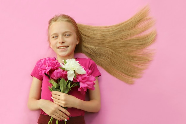 Een meisje met lang blond haar glimlacht met pioenrozen in haar handen