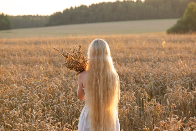 Een meisje met lang blond haar haar rug naar haar toegekeerd met een boeket gerst in het veld Soft focus