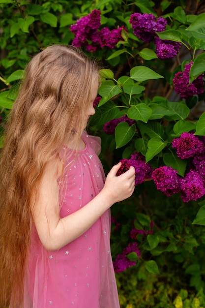 Een meisje met lang blond haar kijkt naar paarse bloemen.