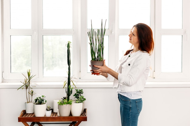 Een meisje met lang haar zorgt voor bloemen, water geven, spuiten, verplanten, pot, groen, raam, thuis