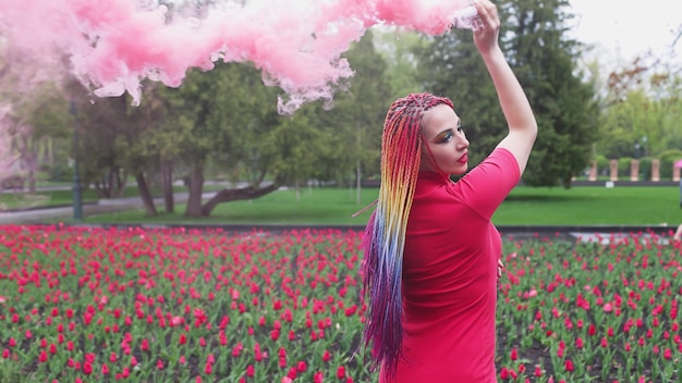 Een meisje met make-up met regenboogvlechten in rode jurk poserend in rode jurk